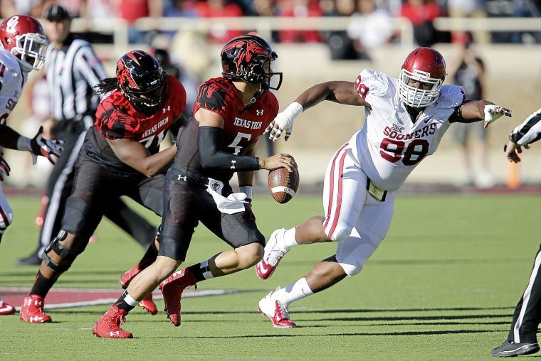 Texas Tech quarterback runs from a player on Oklahomas defense in a past football game. Another Texas Tech player rushes to the quarterbacks side to defend the QB from the OU player.