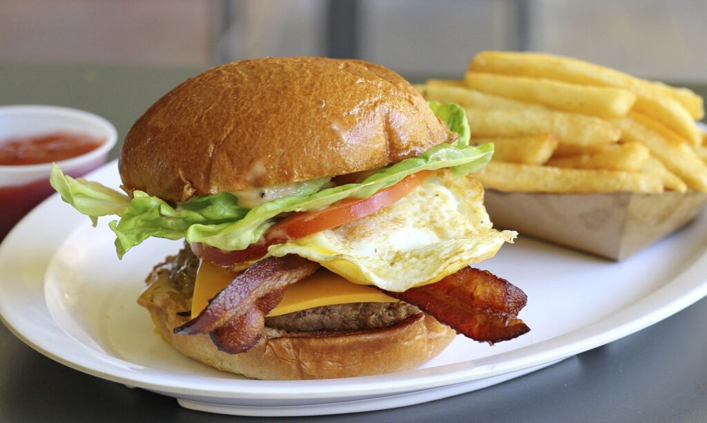 a burger with meat, cheese, bacon, fried egg, tomato, and lettuce, on a bun. With a side of fries. 